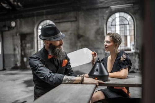 Ein Mann und eine Frau sitzen vor dem Volcano Classic Vaporizer in der Onyx Edition und die Frau hält den Ventilballon